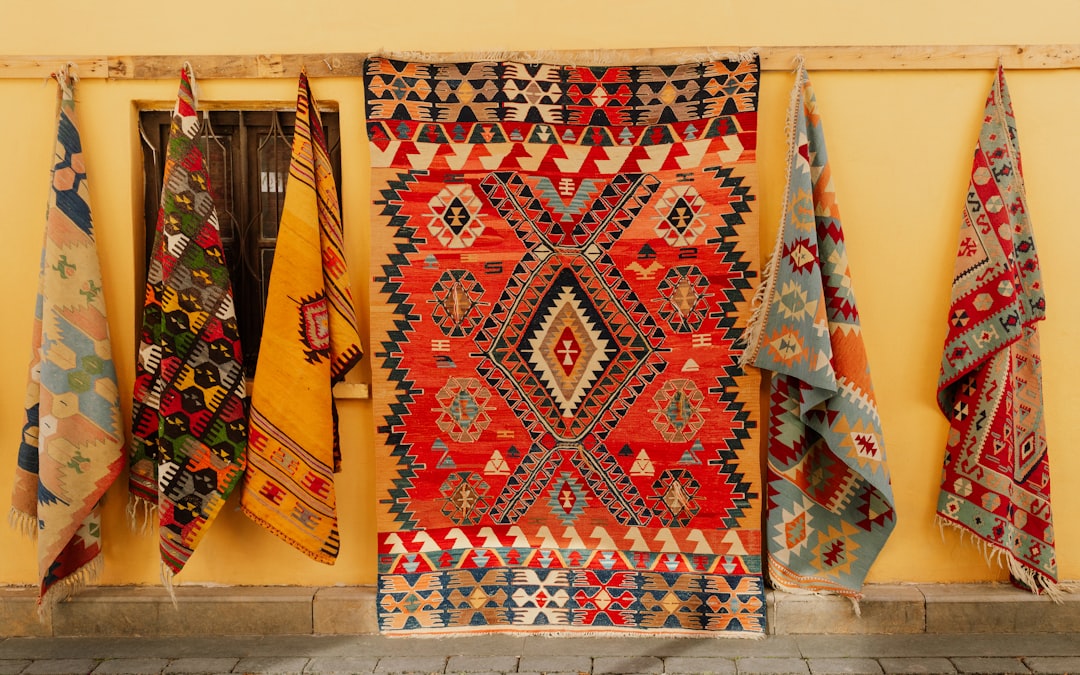Colorful rugs are hanging on a yellow wall.