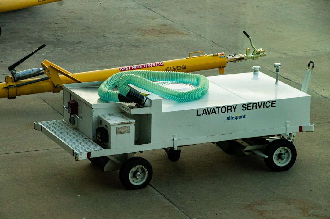 A white lavatory service cart with a green hose on an airport tarmac